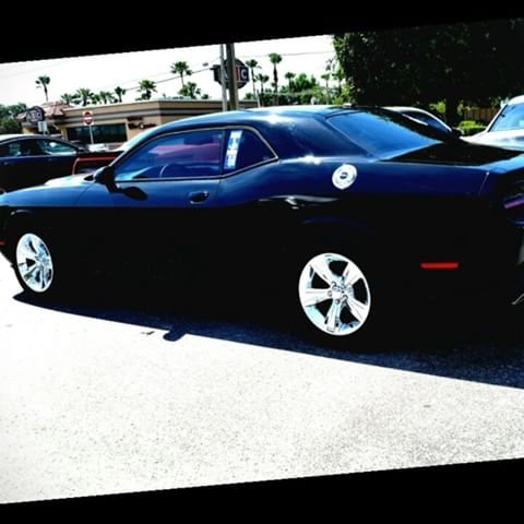 Black Dodge Challenger with chrome five-spoke wheels in a sunny parking lot