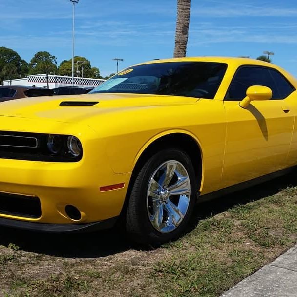 Yellow Dodge Challenger with chrome five-spoke wheels at a Florida dealership
